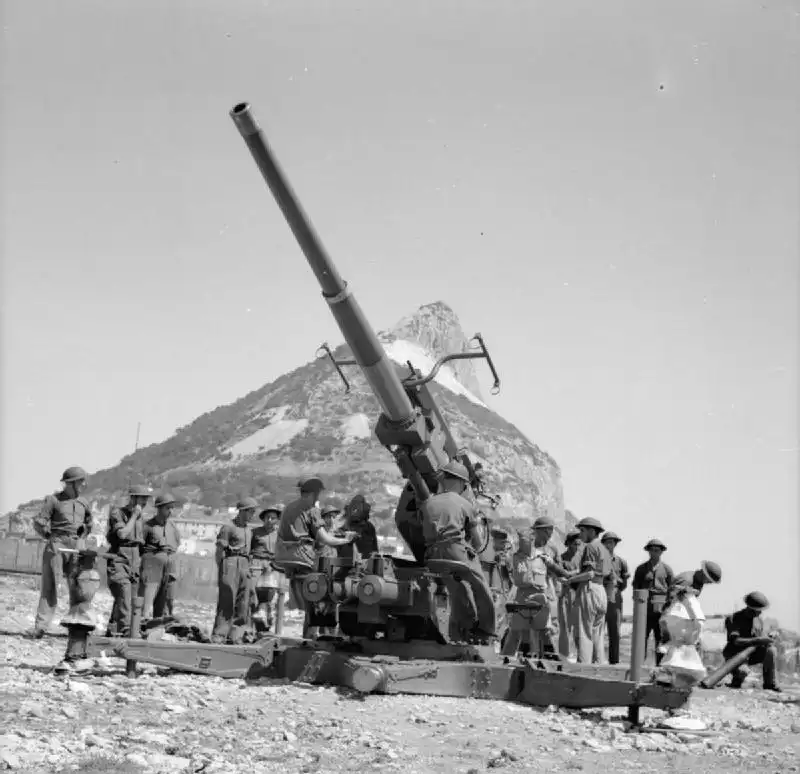 Gibraltar durante la Segunda Guerra Mundial: miembros de la Fuerza de Defensa de Gibraltar operan un cañón antiaéreo de 3,7 pulgadas con el Peñón al fondo.