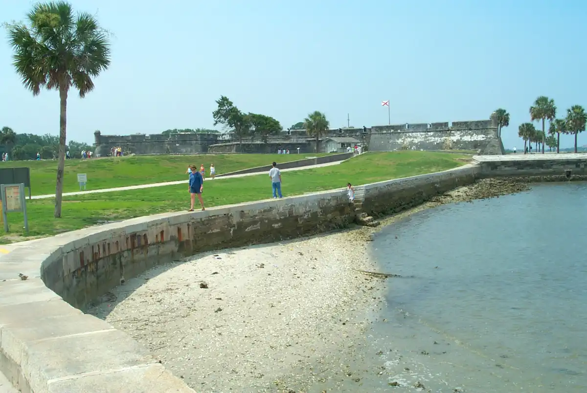 Un visitante camina por el malecón durante la marea baja en el Castillo de San Marcos, con la fortaleza de piedra coquina al fondo. San Agustín, Florida.