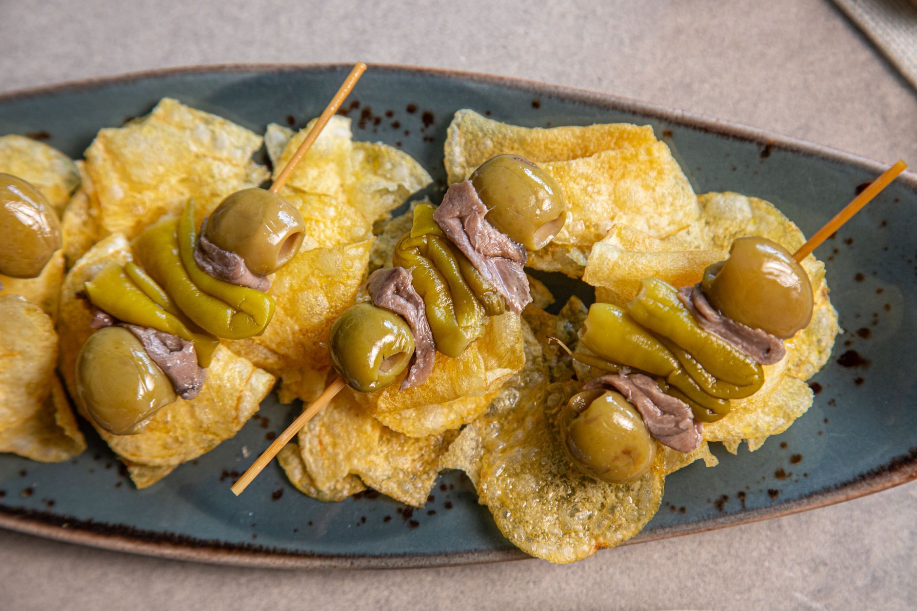traditional basque pintxo skewer olive anchovy chili pepper on bar counter warm light